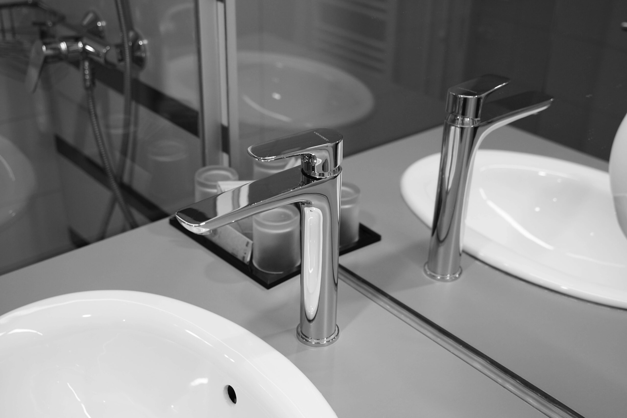 A sleek stainless steel faucet with reflection in a monochrome bathroom setting, emphasizing modern design.