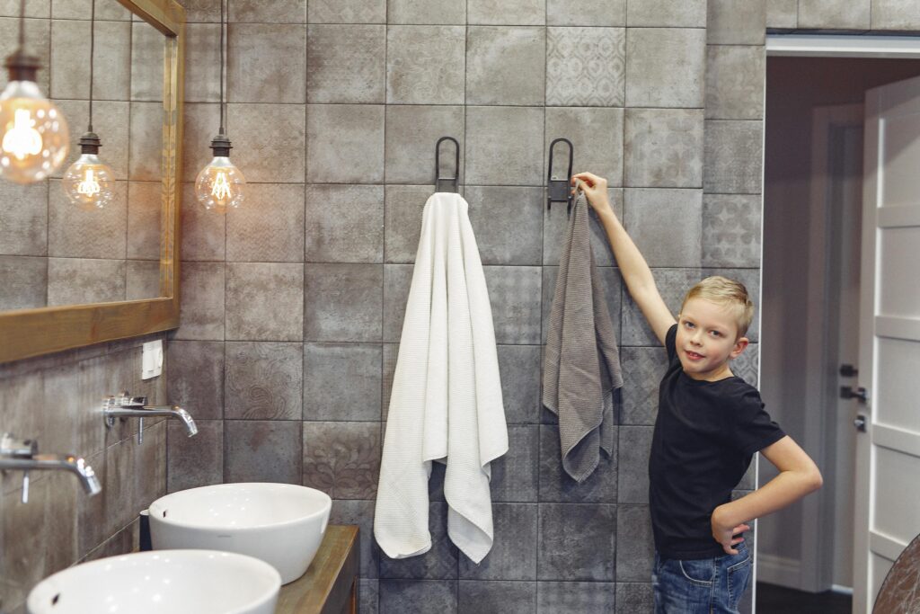 Small boy with blond hair hanging up towel in spacious bathroom while looking at camera